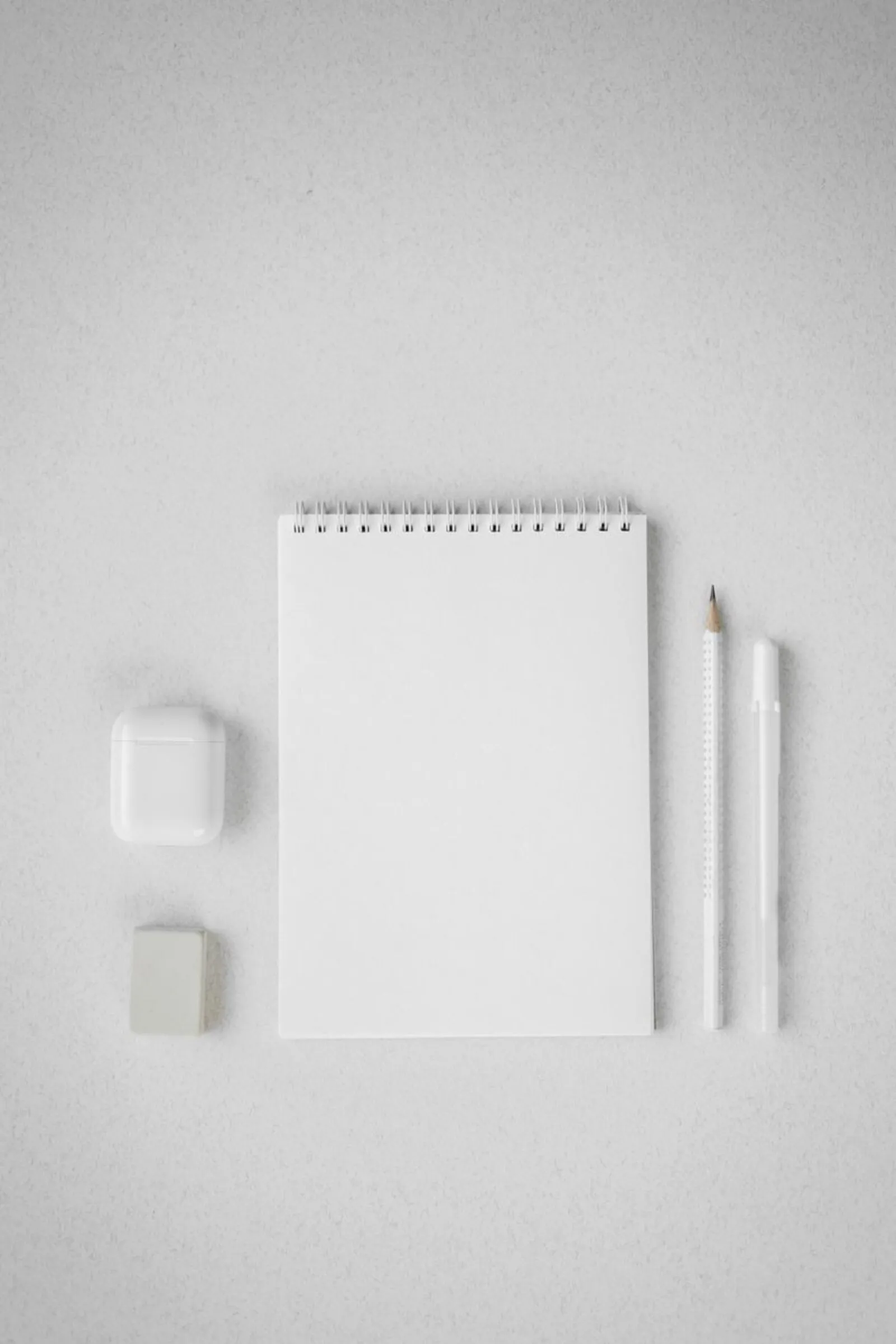 Carnet vierge, crayons et écouteurs posés sur un bureau blanc